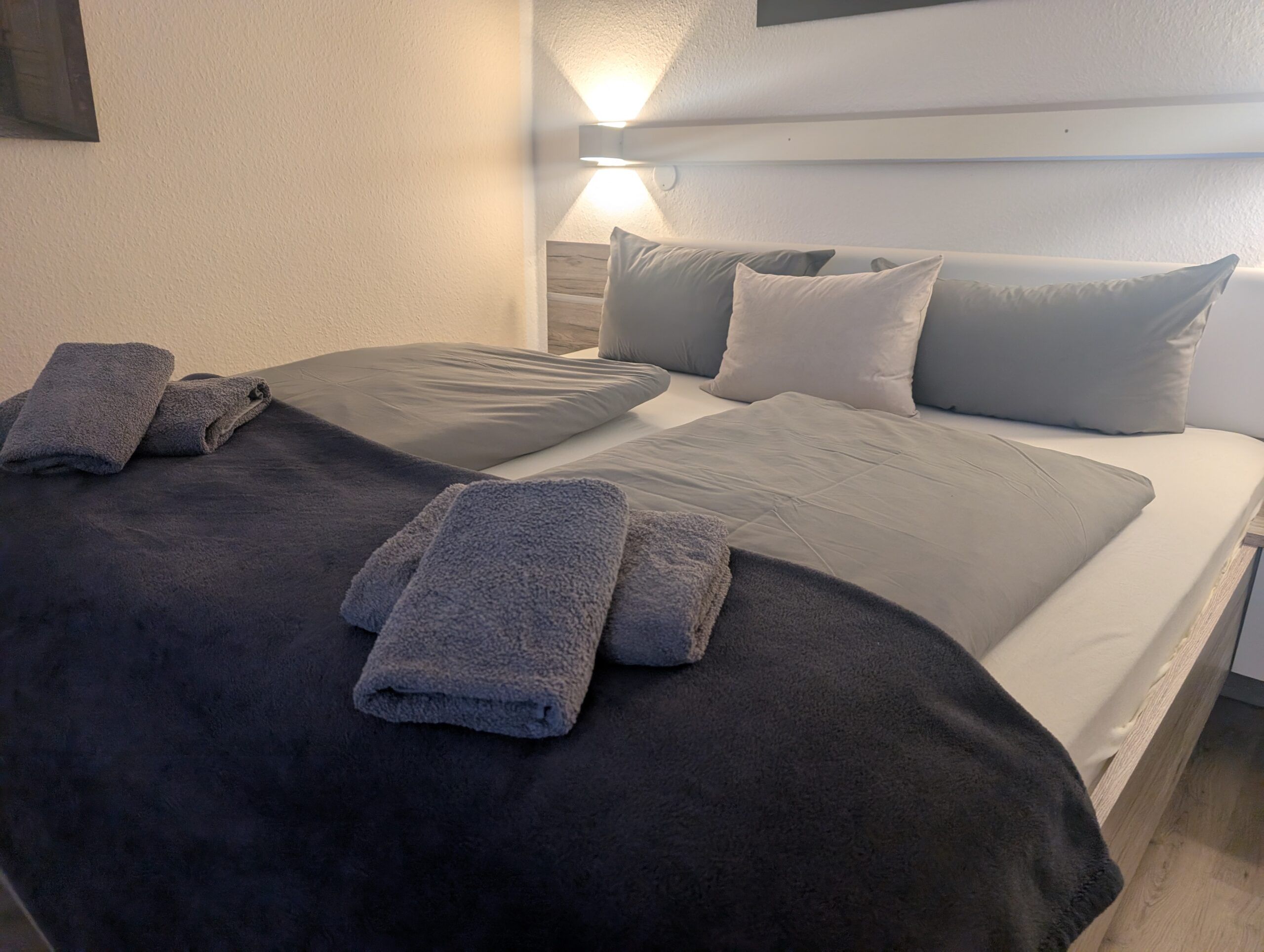 Doppelzimmer mit grauem Kopfteil und gefalteten Handtüchern